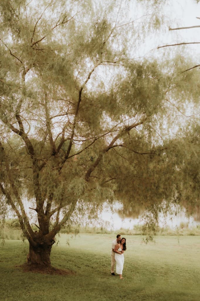 Jaz and Michael smiling under a willow tree by the water
