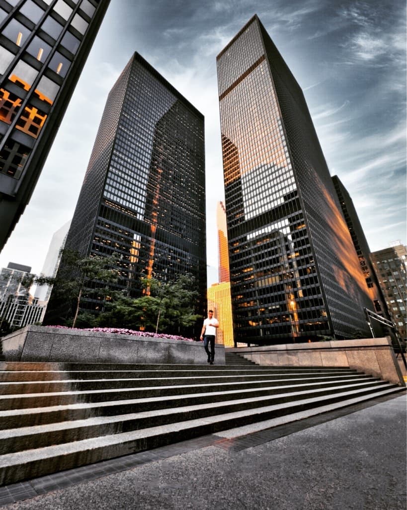 Michael on wide stone steps between glass towers in warm light