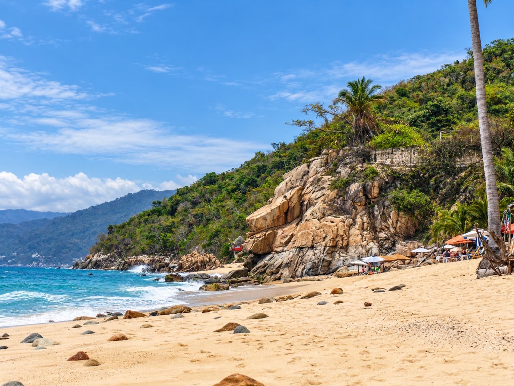 Sandy beach meeting turquoise water and a vegetated cliff