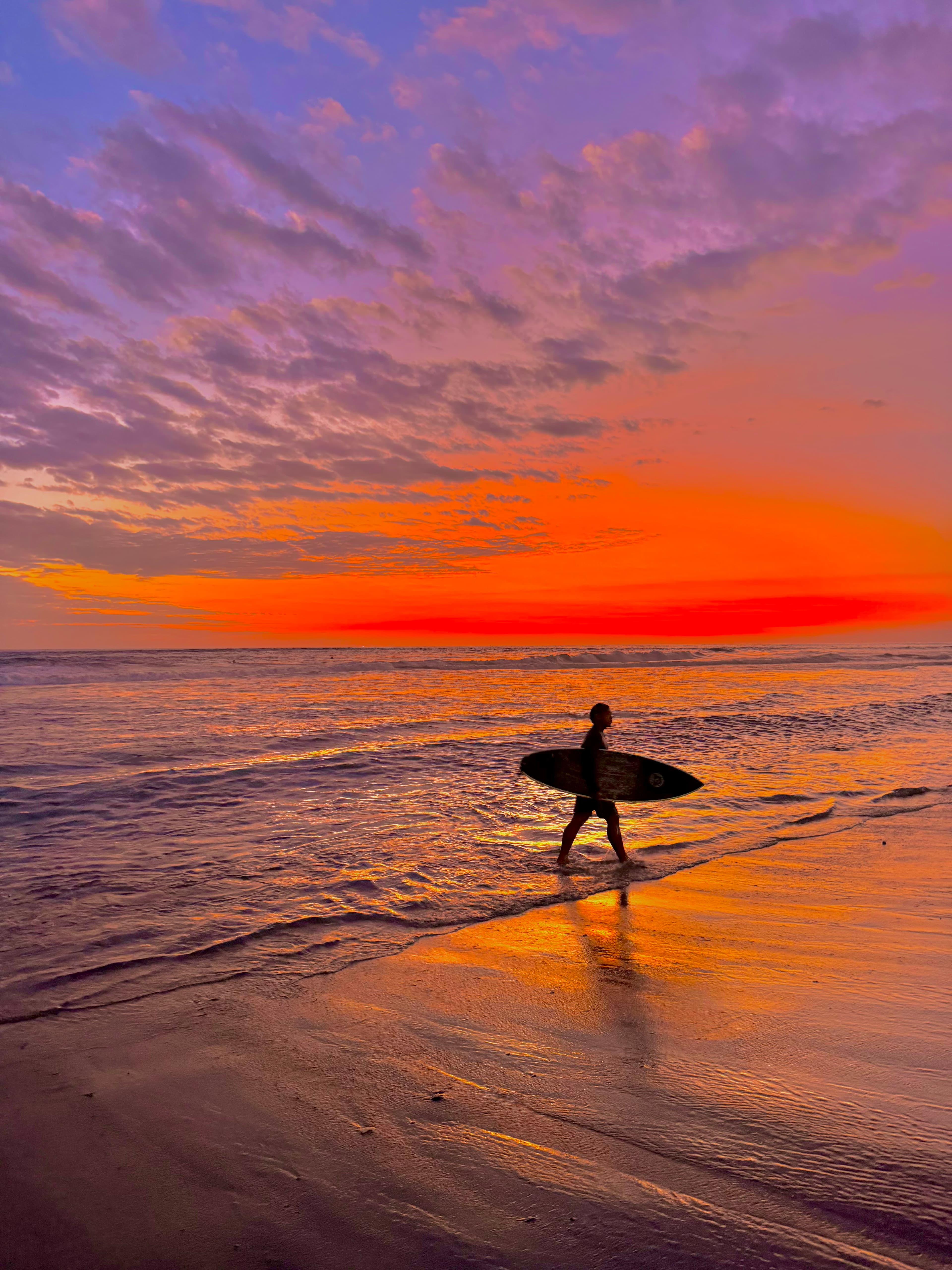 Silhouette with a surfboard along the shore at dusk