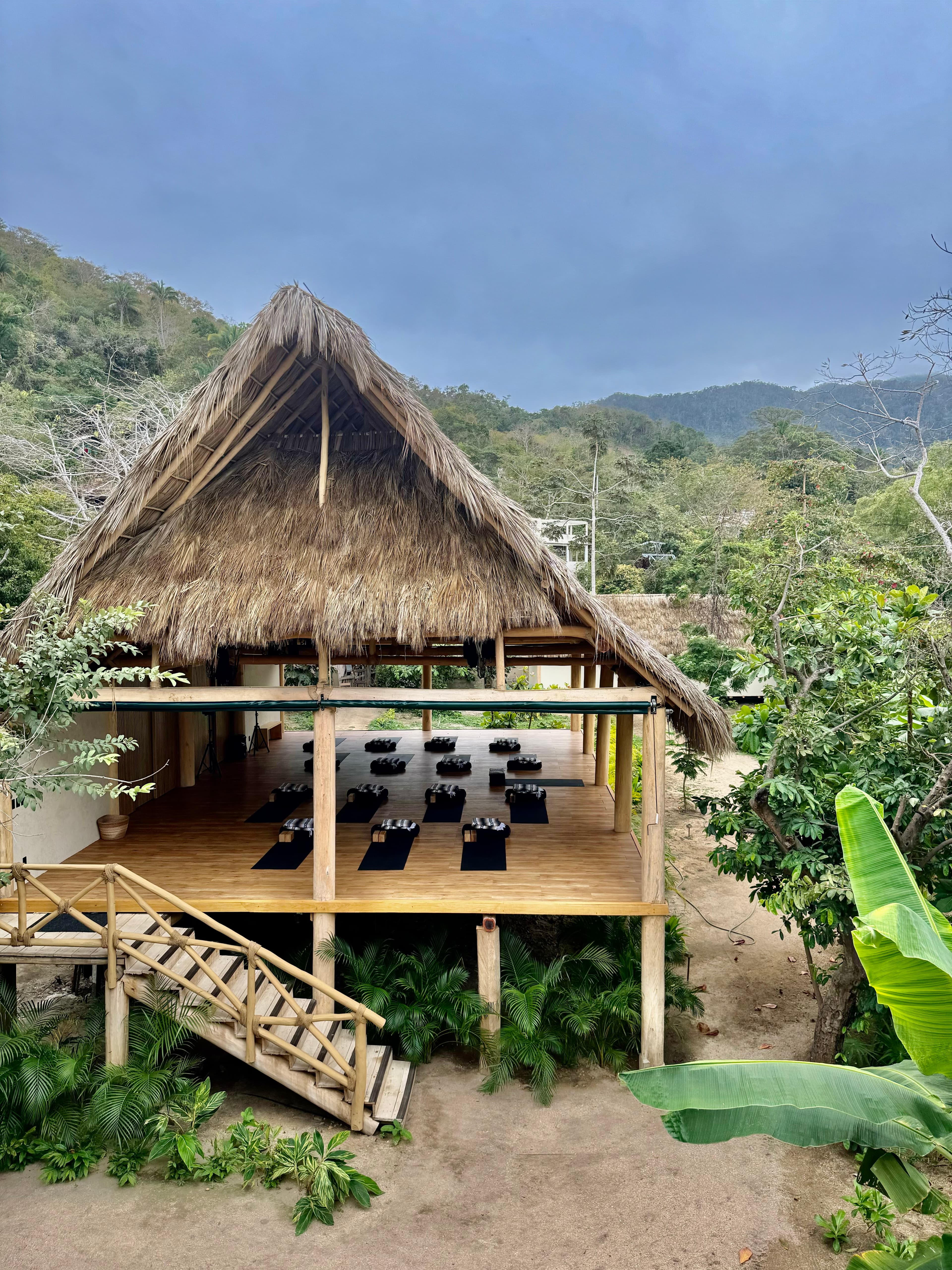 Thatched yoga shala with mats overlooking green hills